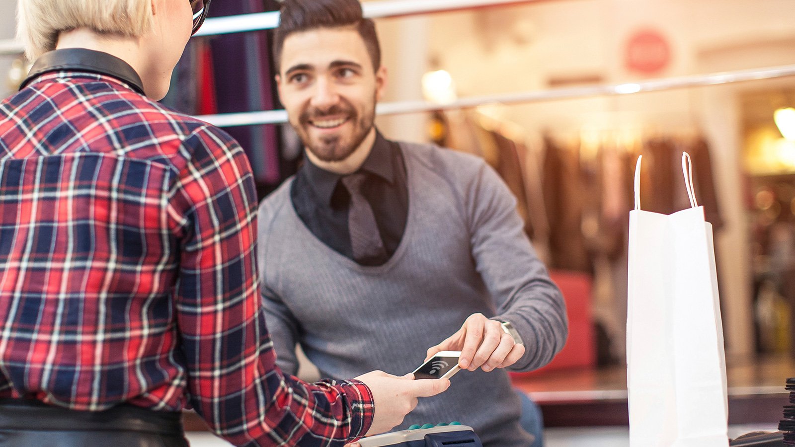 A sales person assisting with a contactless transaction by showing a customer where to hover a mobile phone.