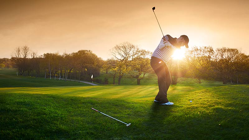 Hombre jugando al golf al atardecer